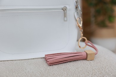 Photo of Stylish backpack with pink leather keychain on soft surface indoors, closeup