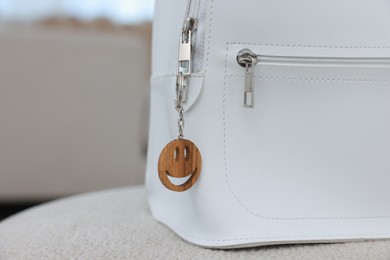 Photo of Stylish backpack with wooden keychain in shape of smiley face on soft surface indoors, closeup