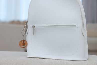 Photo of Stylish backpack with wooden keychain in shape of smiley face on soft surface indoors, closeup