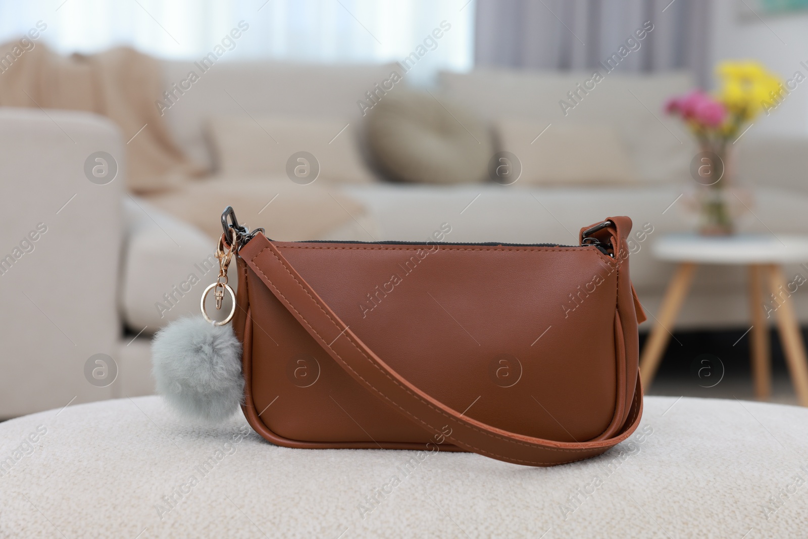 Photo of Stylish bag with faux fur keychain on soft surface indoors, closeup