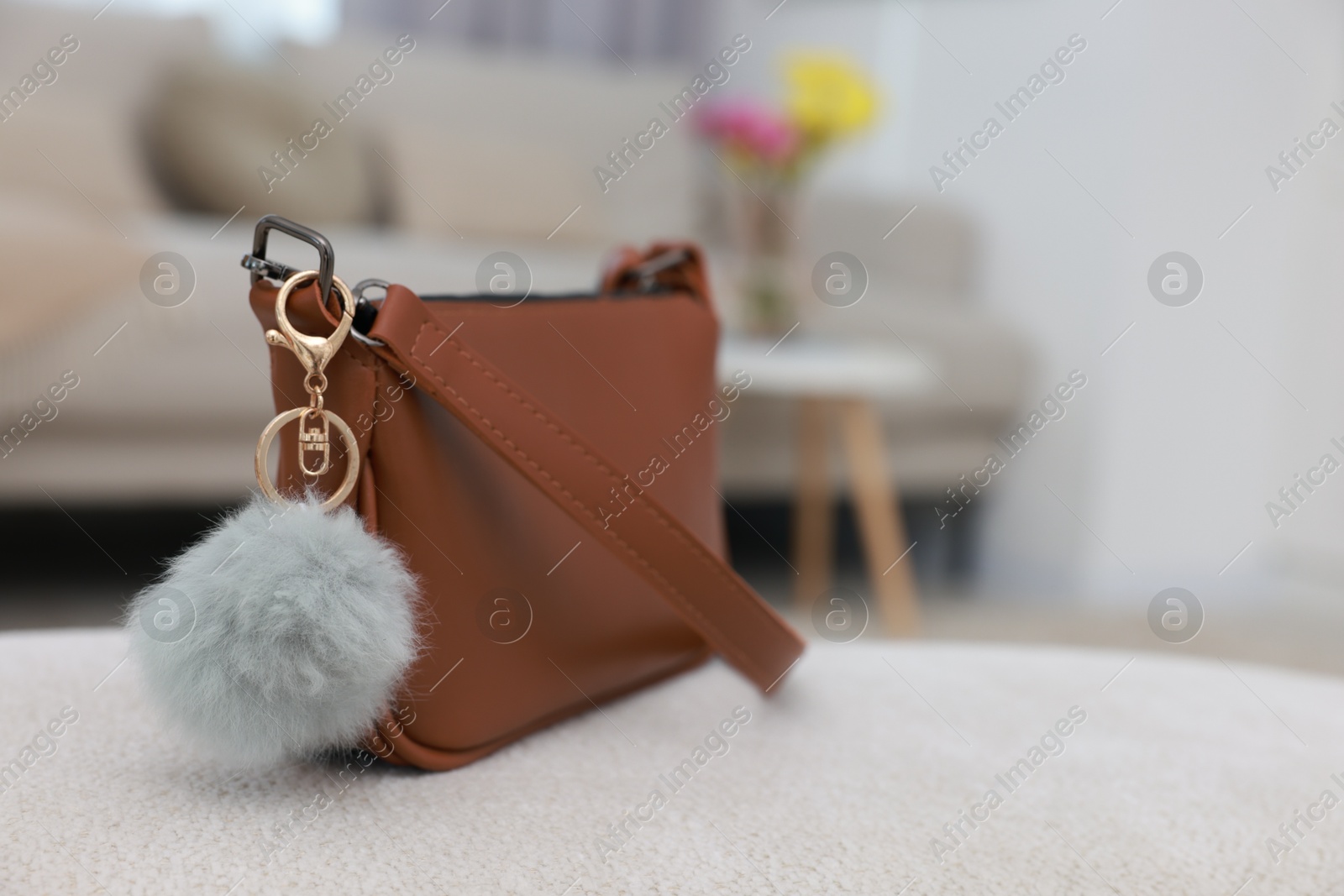 Photo of Stylish bag with faux fur keychain on soft surface indoors, closeup. Space for text