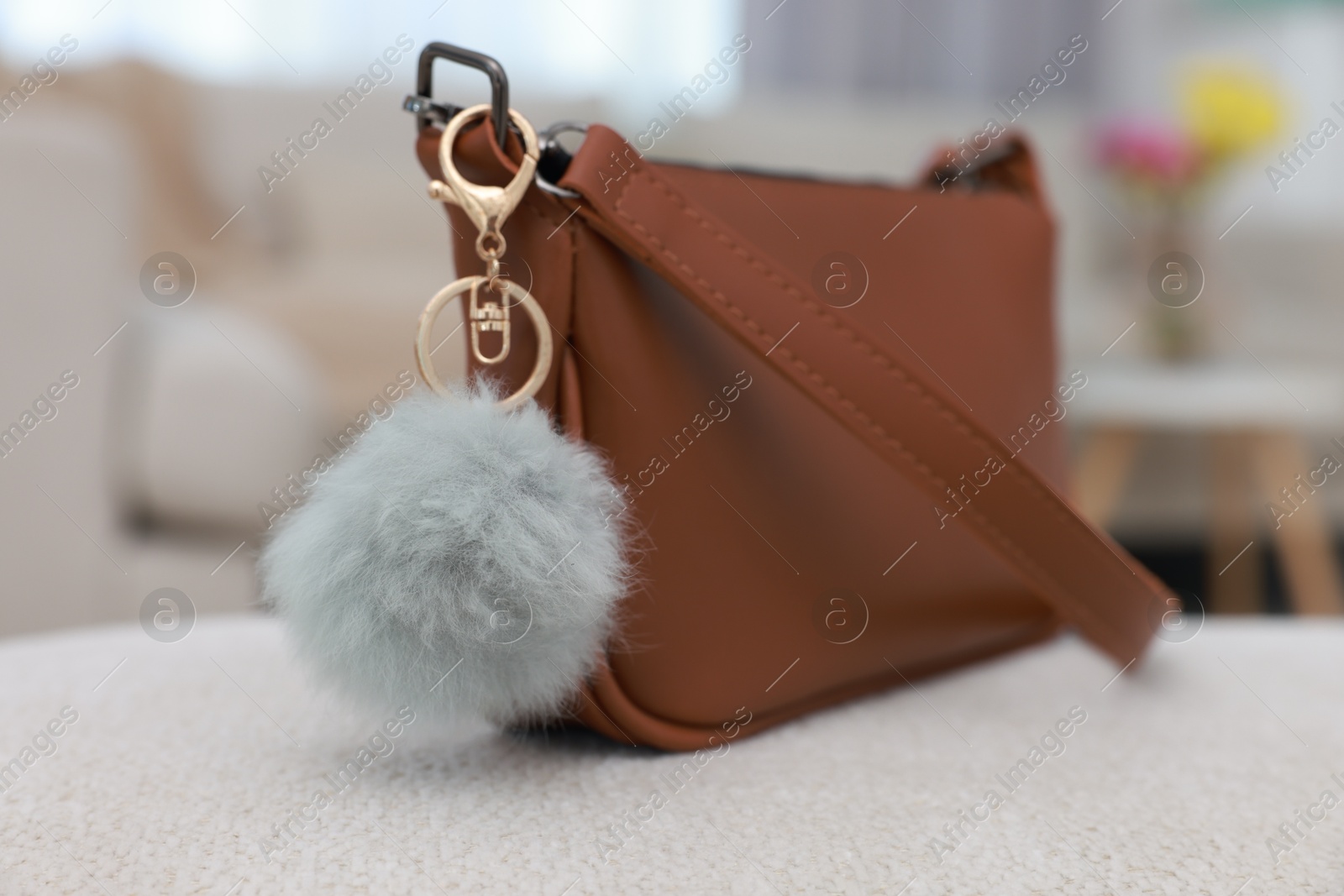 Photo of Stylish bag with faux fur keychain on soft surface indoors, closeup