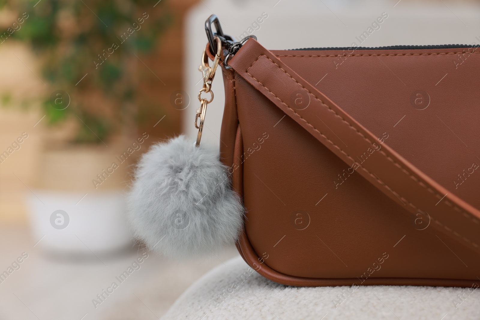 Photo of Stylish bag with faux fur keychain on soft surface indoors, closeup