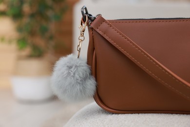 Photo of Stylish bag with faux fur keychain on soft surface indoors, closeup