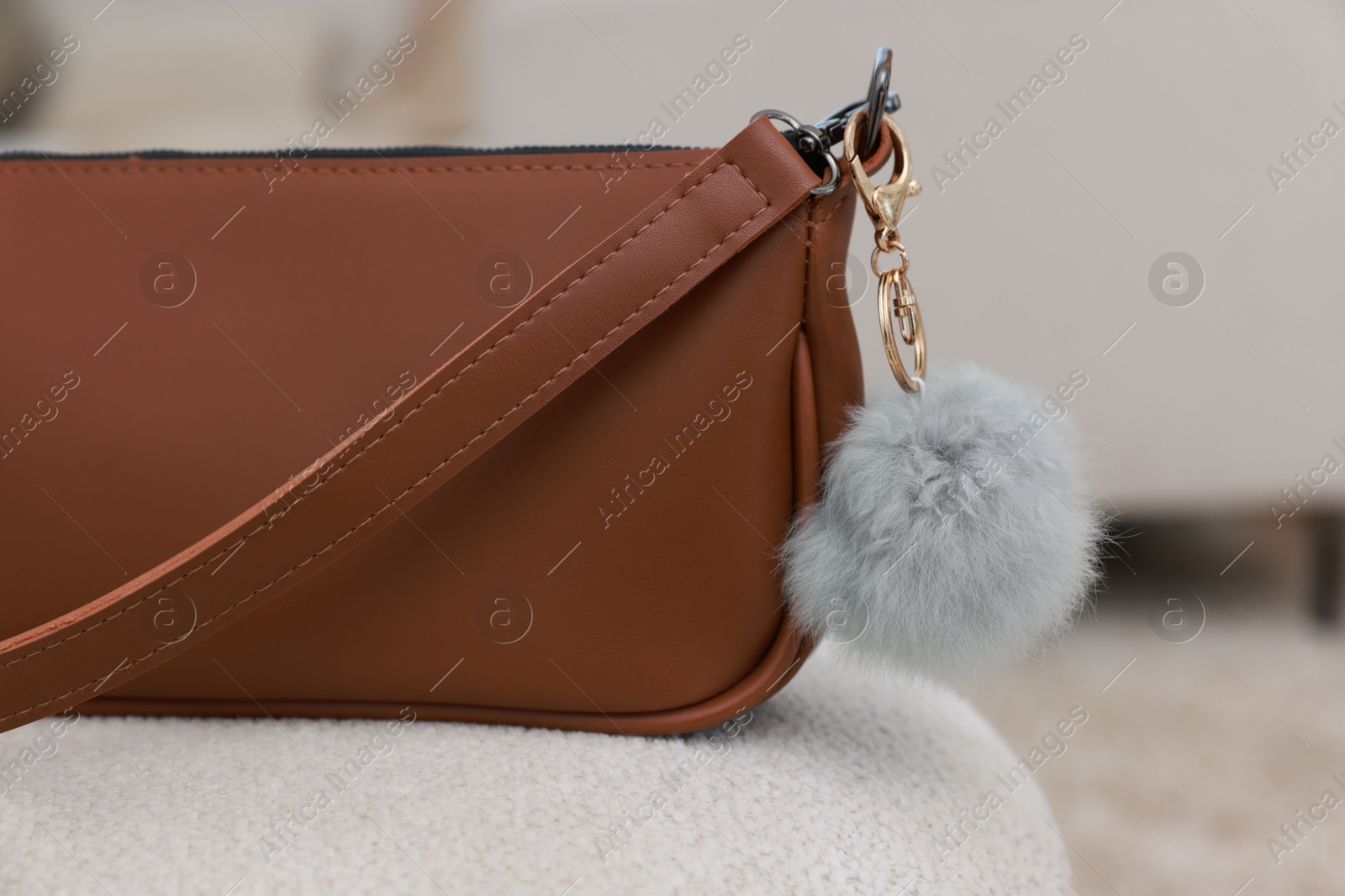 Photo of Stylish bag with faux fur keychain on soft surface indoors, closeup