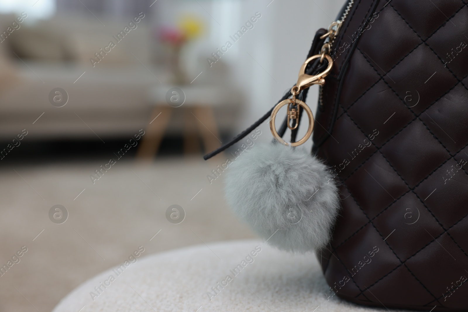 Photo of Stylish backpack with faux fur keychain on soft surface indoors, closeup. Space for text