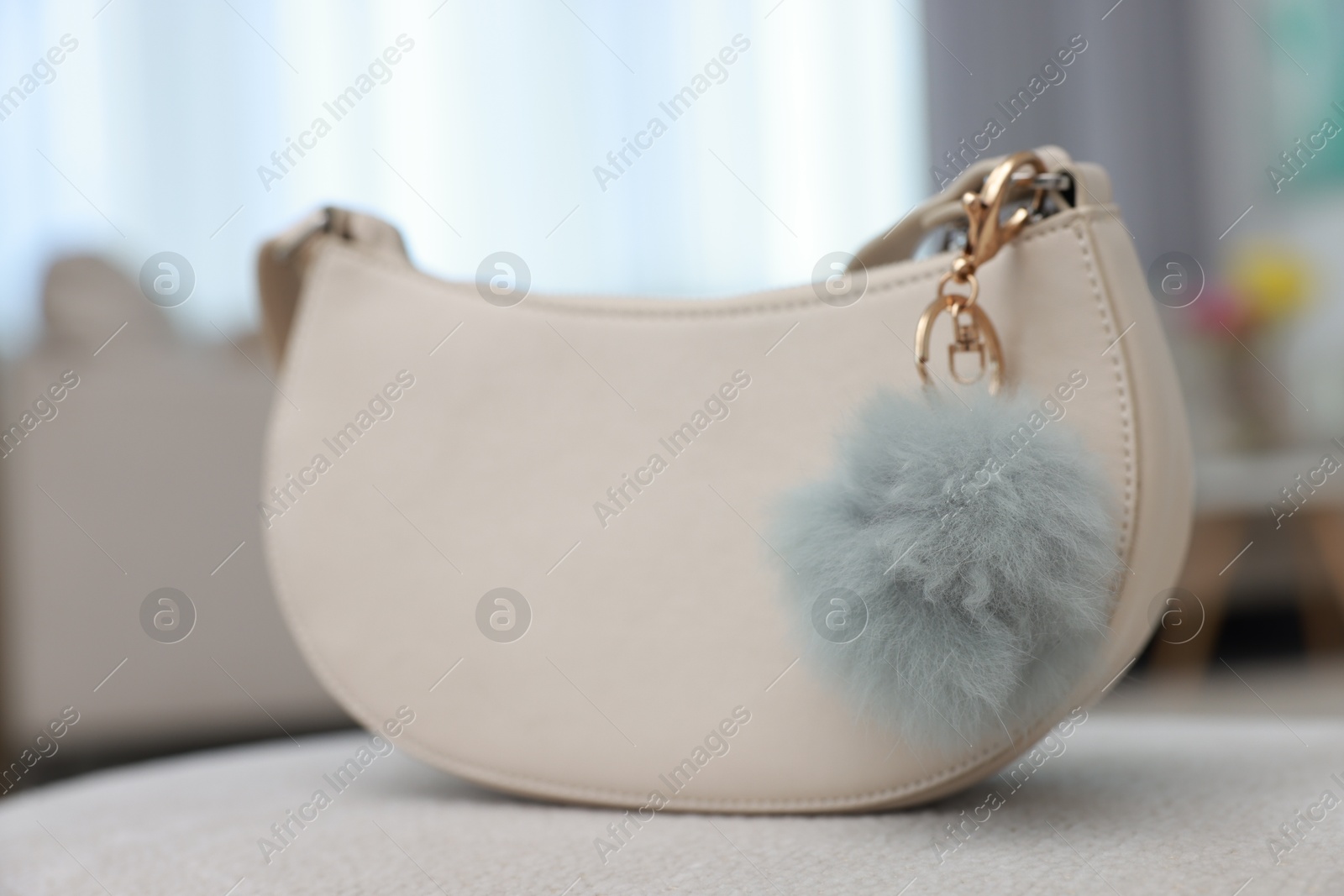 Photo of Stylish bag with faux fur keychain on soft surface indoors, closeup