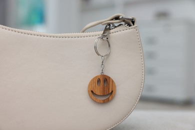 Photo of Stylish bag with wooden keychain in shape of smiley face indoors, closeup