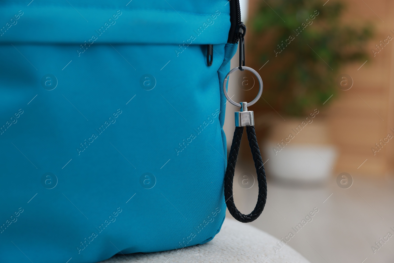 Photo of Backpack with black leather keychain on soft surface indoors, closeup. Space for text