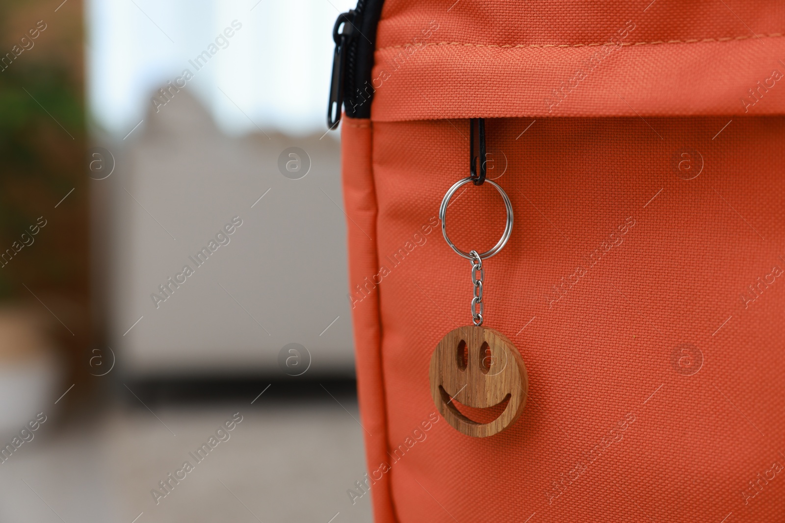 Photo of Backpack with wooden keychain in shape of smiley face on blurred background, closeup. Space for text