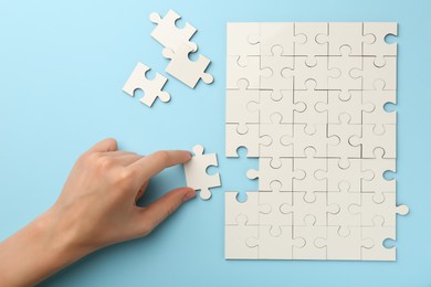 Photo of Woman solving white puzzle on light blue background, closeup