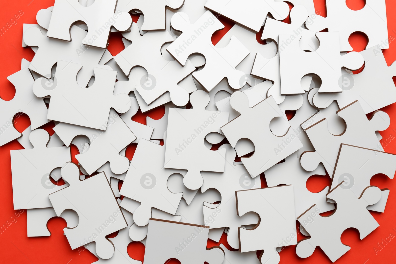 Photo of Pile of white puzzle pieces on red background, closeup