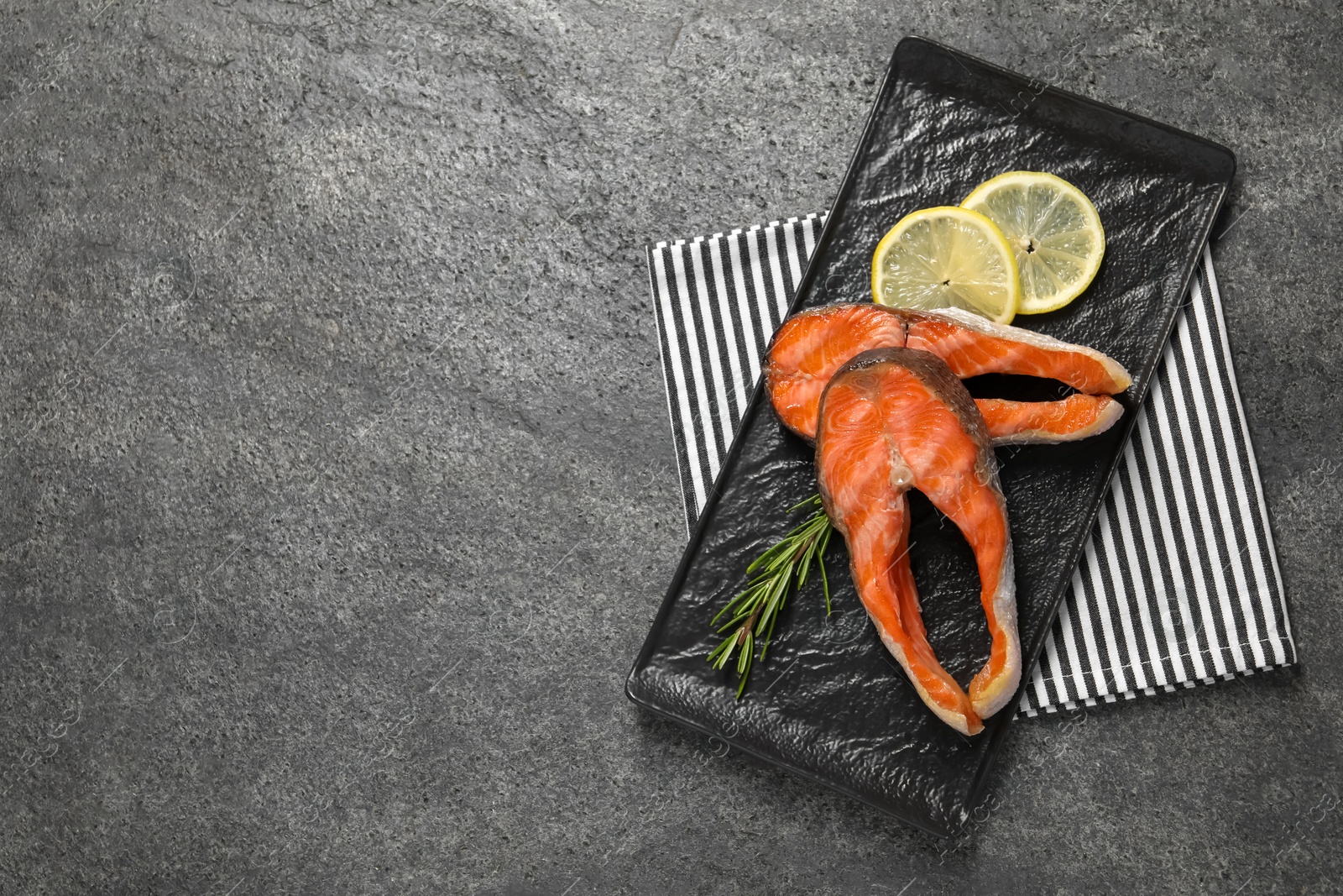 Photo of Tasty grilled salmon steaks, lemon and rosemary on gray textured table, top view. Space for text