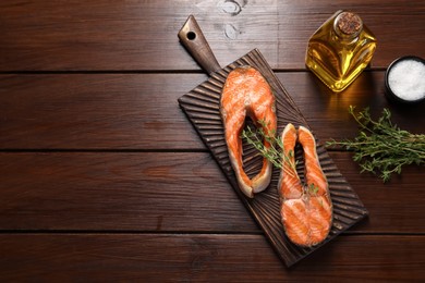 Photo of Tasty grilled salmon steaks, oil and spices on wooden table, flat lay. Space for text