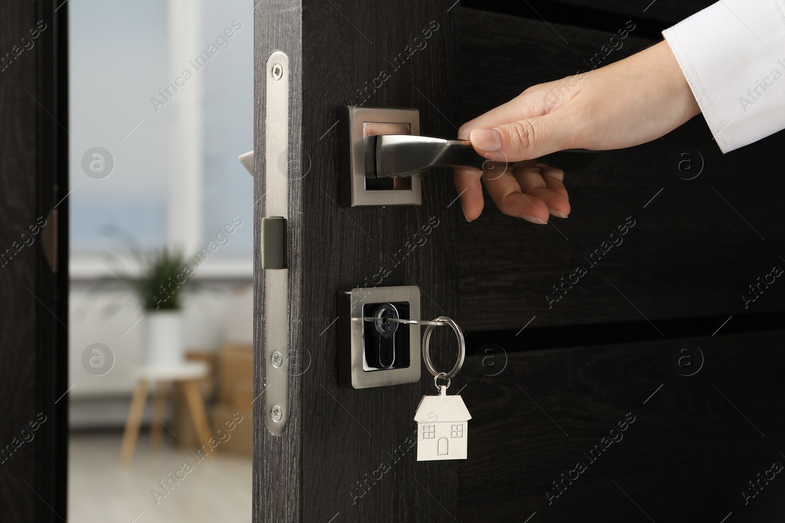 Photo of Woman opening door with key and house shaped keychain, closeup