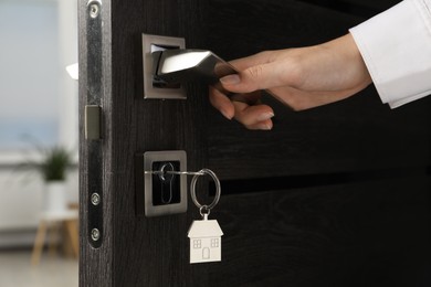 Photo of Woman opening door with key and house shaped keychain, closeup