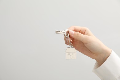 Woman holding key with keychain on light grey background, closeup. Space for text