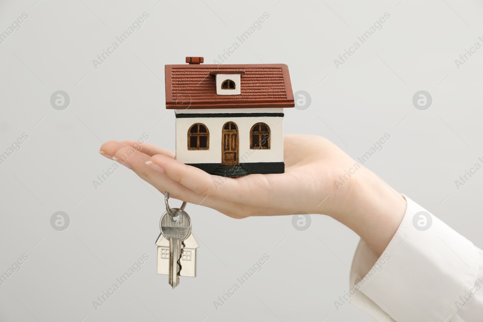 Photo of Woman holding key with keychain and house model on light grey background, closeup