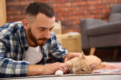 Man petting cute ginger cat on floor at home