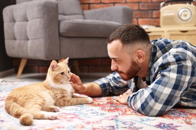 Photo of Man petting cute ginger cat on floor at home