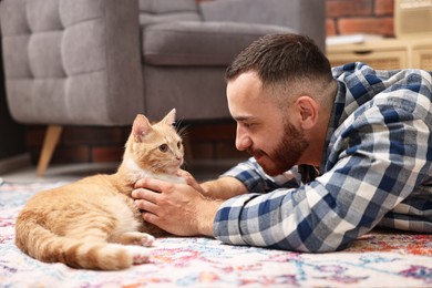 Man petting cute ginger cat on floor at home