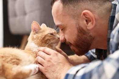 Man petting cute ginger cat on floor at home