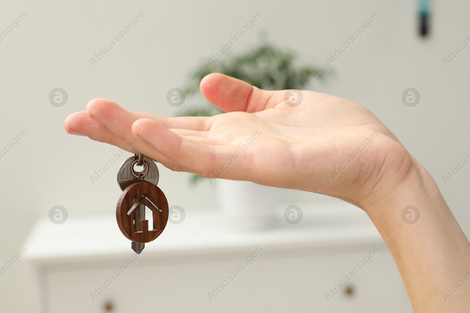 Photo of Woman holding key with house shaped keychain indoors, closeup