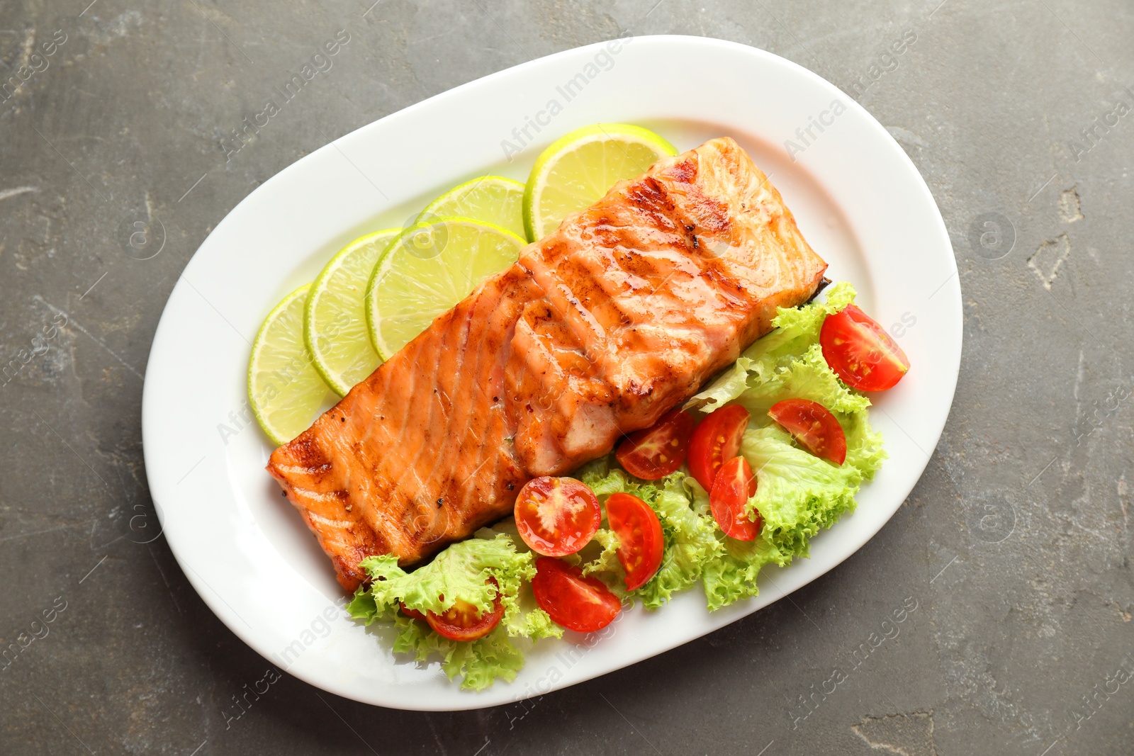 Photo of Delicious grilled salmon fillet with vegetable salad and lime on grey textured table, top view