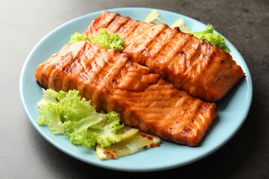 Photo of Delicious grilled salmon fillets with lettuce and lemon on grey table, closeup