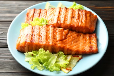 Photo of Delicious grilled salmon fillets with lettuce and lemon on wooden table, closeup