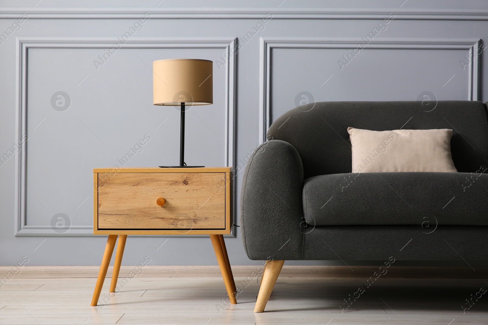 Photo of Stylish sofa with cushion and lamp on side table near grey wall