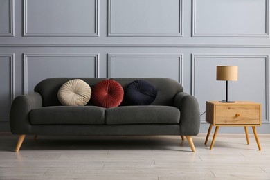 Photo of Stylish sofa with cushions and lamp on side table near grey wall