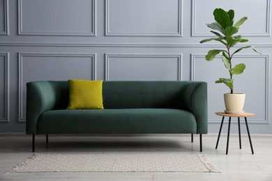 Photo of Stylish sofa with cushion and green plant on side table near grey wall