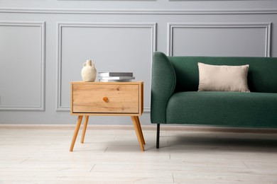 Photo of Stylish sofa with cushion and books on side table near grey wall