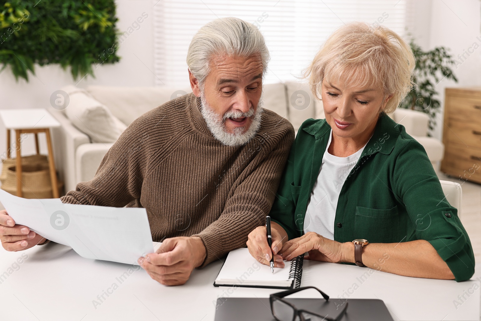 Photo of Pension savings. Senior couple planning budget at white table indoors