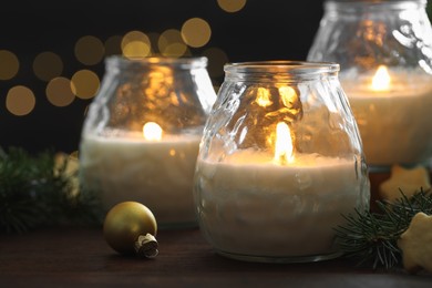 Photo of Burning candles, baubles and fir tree branches on wooden table, closeup