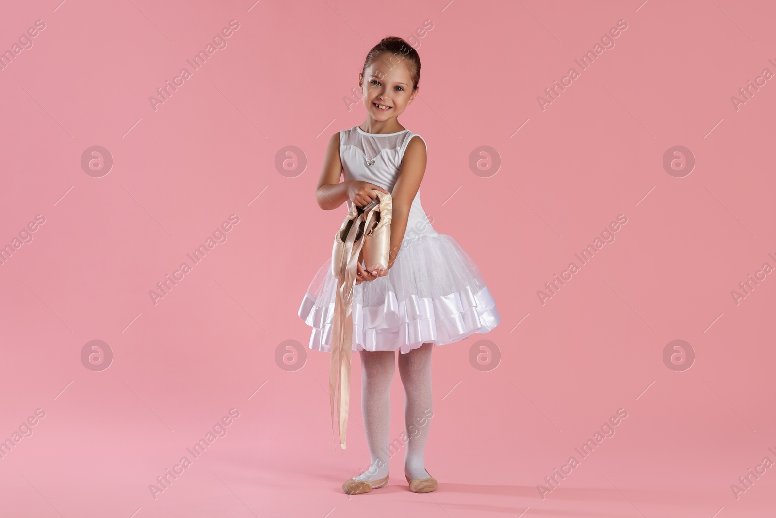 Photo of Little ballerina with pointe shoes on pink background