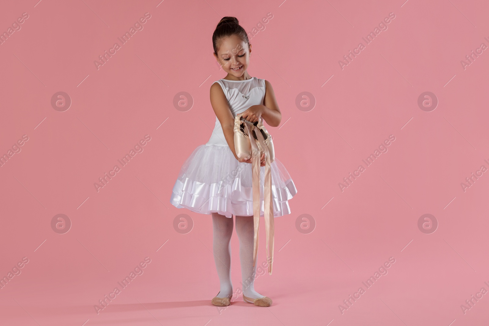 Photo of Little ballerina with pointe shoes on pink background