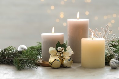 Photo of Burning candles, baubles and fir tree branches on white textured table, closeup