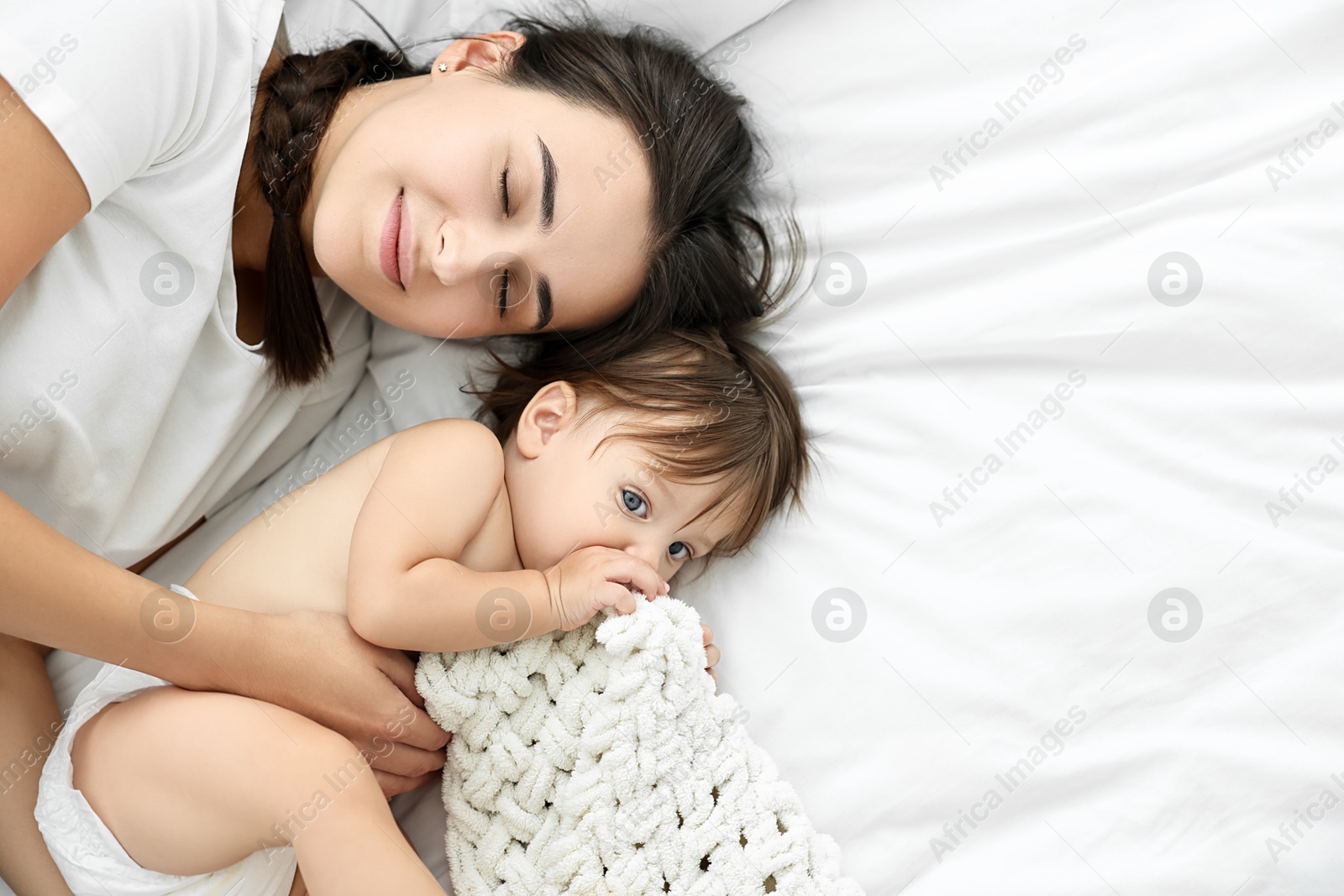 Photo of Beautiful young mother with her cute little baby on bed, top view