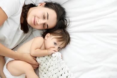 Photo of Beautiful young mother with her cute little baby on bed, top view