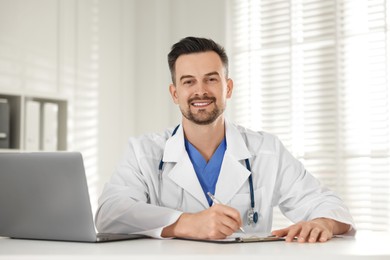 Smiling doctor with clipboard at table in clinic