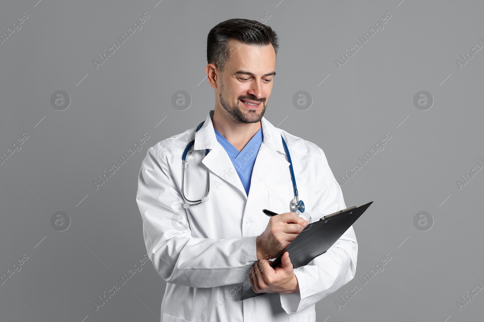 Photo of Smiling doctor with stethoscope and clipboard on grey background