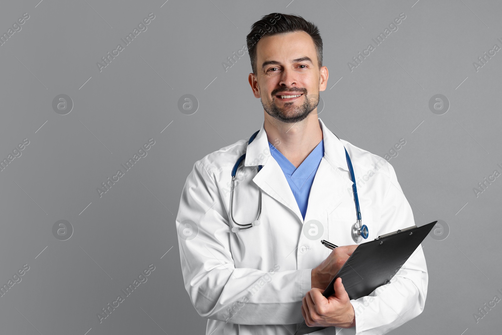 Photo of Smiling doctor with stethoscope and clipboard on grey background, space for text