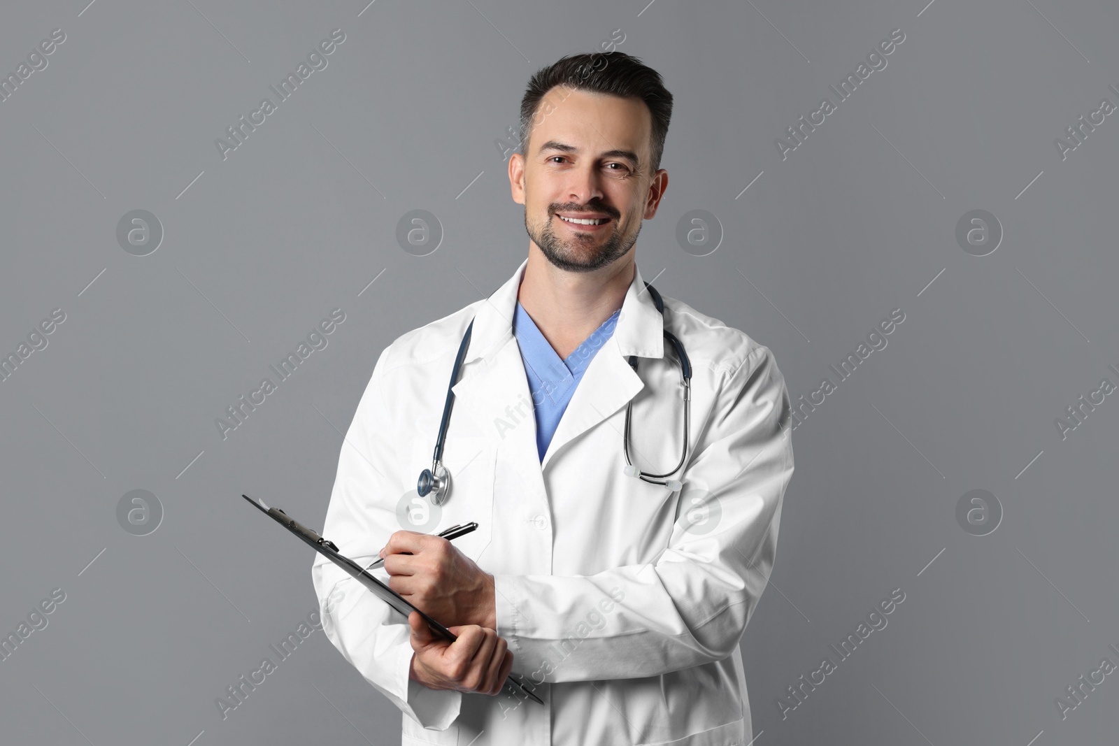 Photo of Smiling doctor with stethoscope and clipboard on grey background