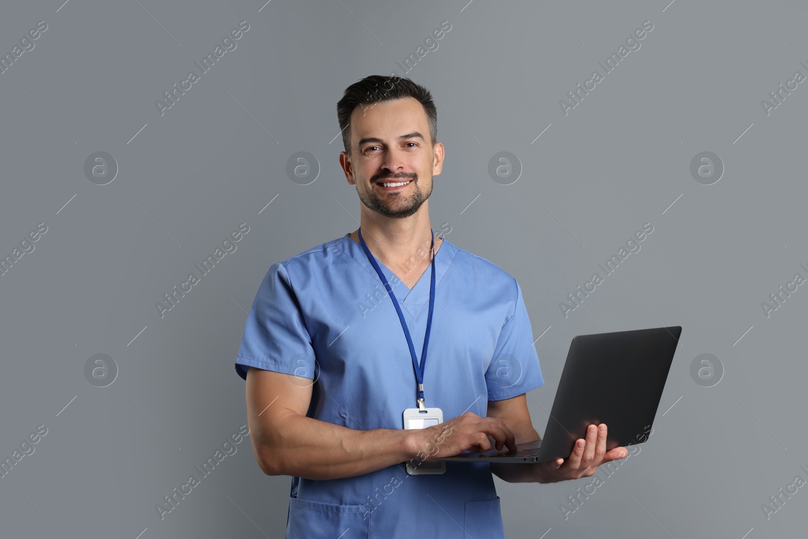 Photo of Smiling nurse with badge and laptop on grey background