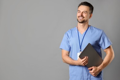 Smiling nurse with badge and laptop on grey background, space for text