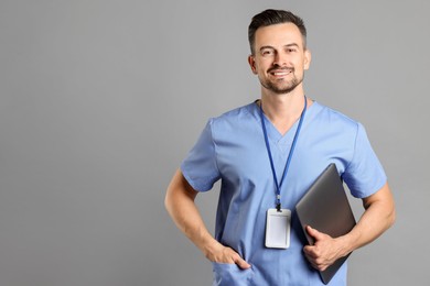 Photo of Smiling nurse with badge and laptop on grey background, space for text