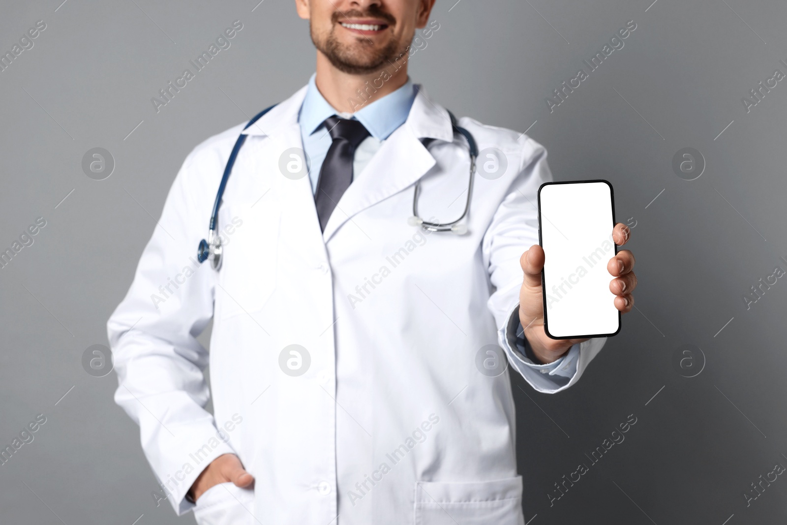 Photo of Doctor showing smartphone with blank screen on grey background, closeup. Mockup for design