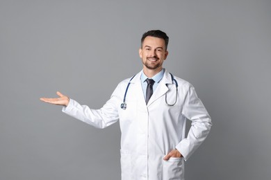 Photo of Smiling doctor with stethoscope pointing at something on grey background